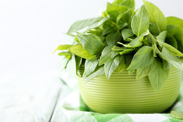 Basil leaves in bowl white wooden background