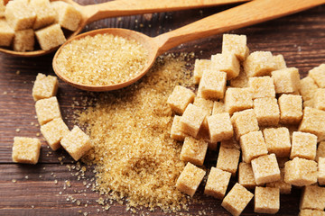 Brown sugar in spoon and bowl on wooden background