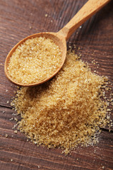 Brown sugar in spoon and bowl on wooden background