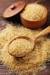 Brown sugar in spoon and bowl on wooden background