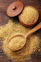 Brown sugar in spoon and bowl on wooden background