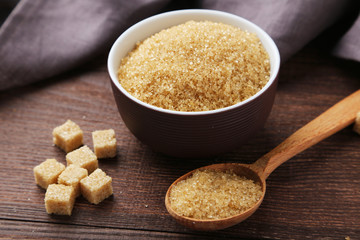 Brown sugar in spoon and bowl on wooden background