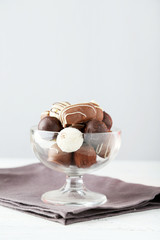 Chocolates in glass on white wooden background