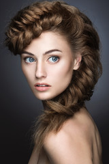 Beautiful girl with light make-up, perfect skin and hairstyle as a braid. Picture taken in the studio on a gray background