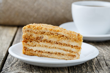 Tasty honey cake with cup of coffee on wooden background.