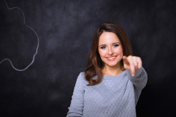 Young cute smiling girl pointing at you isolated on gray