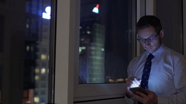 Businessman using smartphone at night next to the window
