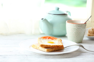 Scrambled egg with bread on plate with cup of tea on bright background