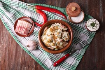 Fried dumplings with onion and bacon in frying pan, on wooden table background