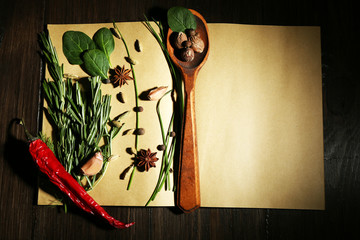 Open recipe book with fresh herbs and spices on wooden background