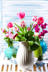 Different beautiful flowers in vases on wooden background