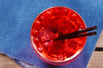 Glass of compote with red currant on wooden table with jeans cloth, closeup