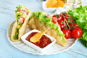 Tasty taco with tomato dip on plate and vegetables on table close up