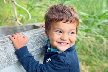 Child with his hands clinging to a well turns to watch his friends smiling
