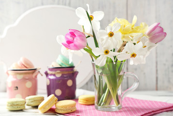 Obraz na płótnie Canvas Spring bouquet in glass mug and tasty macaroons on color wooden background