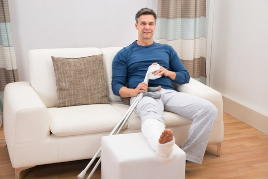 Man Sitting On Sofa With Crutches