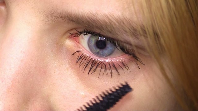 young girl apply mascara on left eye, closeup