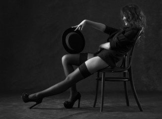 Sexy young woman sitting on a chair on a black background. - obrazy, fototapety, plakaty