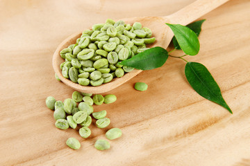 Fototapeta na wymiar Green coffee beans in spoon and leaves on wooden background