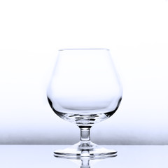 An empty cognac snifter in slightly blue light with a reflection