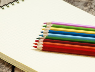 Workspace with colored pencils and notebook on old wooden table