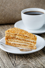 Tasty honey cake with cup of coffee on wooden background.