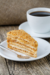 Tasty honey cake with cup of coffee on wooden background.