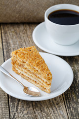 Tasty honey cake with cup of coffee on wooden background.