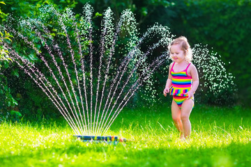 Little girl playing with garden water sprinkler