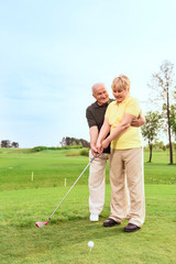 Old man teaching his wife to play golf