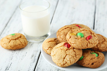 Cookies with colorful candy in plate on white wooden background
