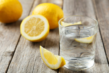 Lemons with glass of water on grey wooden background