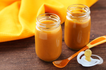 Baby food in bottles with spoon on brown wooden background