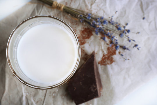 Glass of milk with chocolate chunks and dried flower on sheet of crumpled paper on white background