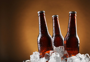 Glass bottles of beer in ice cubes on color background