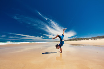 Acrobatic young boy performing hand stand on the beach