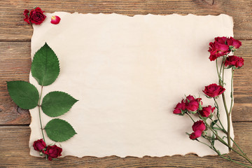 Dried roses on sheet of paper on wooden table, top view