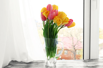 Beautiful bouquet of tulips in carafe on windowsill