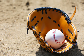 Baseball ball and glove on sand