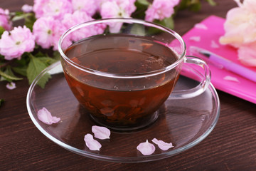 Cup of herbal tea with pink roses on wooden table, closeup