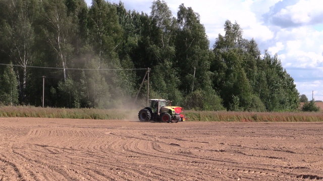 Tractor spread fertilizer on cultivated field near forest