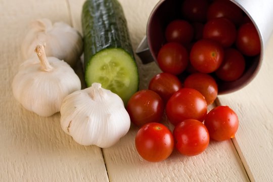 Several cherry tomatoes and garlic with cucumber on white board