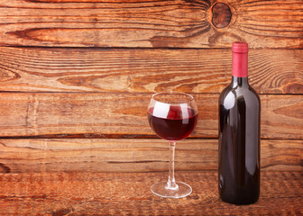 Glass of red wine and bottle on wooden table