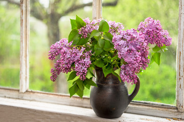 Lush bouquet of lilac in a brown clay vase on a window sill