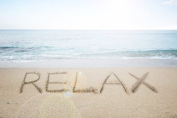 Relax word handwritten in sand on sunny beach