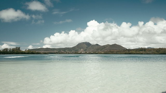 beach at ile aux cerf in mauritius with mountains and clouds in the background. boat passing