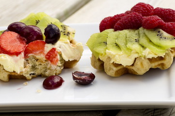 Two fresh summer fruit and cream waffles, one half eaten.  