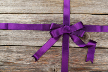 Purple ribbon with bow on grey wooden background