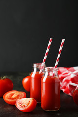 Fresh red tomatoes and juice in bottles on black background