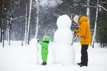 Son and father make two snowmans in park. 
